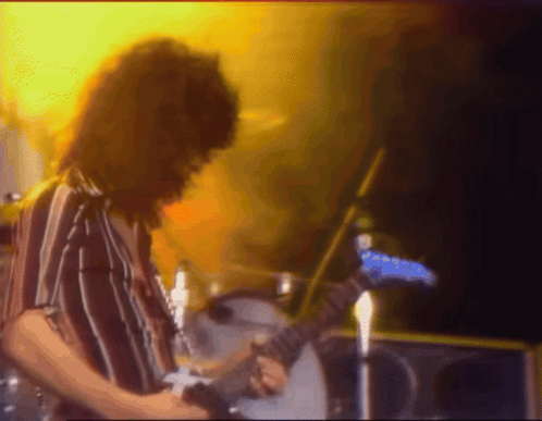 A Man In A Striped Shirt Is Playing A Guitar On Stage GIF