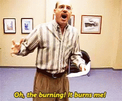 A Man In A Striped Shirt Is Saying Oh The Burning It Burns Me While Holding A Piece Of Paper GIF