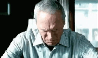 A Man In A Striped Shirt Is Sitting At A Table With His Head Down . GIF