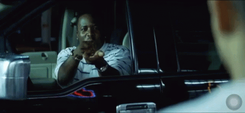 A Man In A Striped Shirt Is Sitting In A Car And Pointing At Something GIF