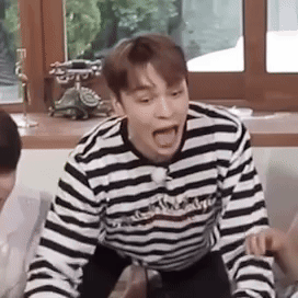 A Man In A Striped Shirt Is Sitting On A Couch With His Mouth Open And Making A Funny Face . GIF