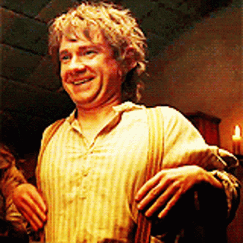 A Man In A Striped Shirt Is Smiling In A Dark Room With A Candle In The Background . GIF