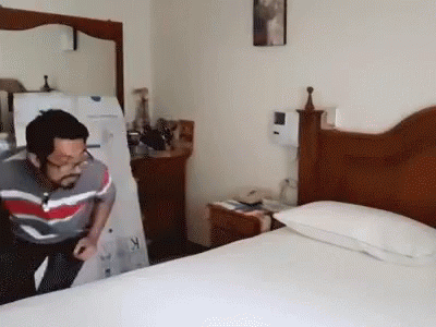 A Man In A Striped Shirt Is Standing In A Bedroom Next To A Bed GIF