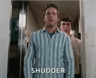 A Man In A Striped Shirt Is Standing In A Hallway With Another Man Behind Him . GIF