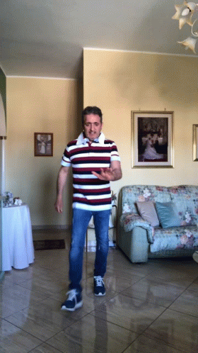 A Man In A Striped Shirt Is Standing In A Living Room In Front Of A Couch GIF