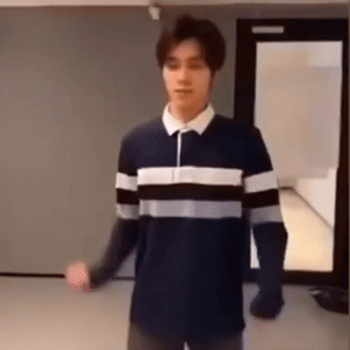 A Man In A Striped Shirt Is Standing In A Room . GIF