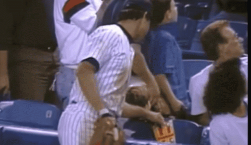 A Man In A Striped Shirt Is Standing In A Stadium Holding A Bag Of Chips GIF