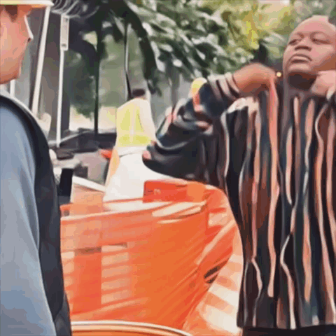 A Man In A Striped Shirt Is Standing In Front Of A Construction Site GIF