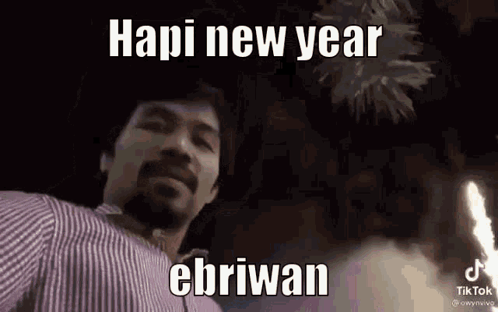 A Man In A Striped Shirt Is Standing In Front Of A Fireworks Display And Says Hapi New Year Ebriwan . GIF
