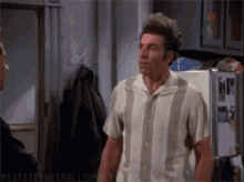 A Man In A Striped Shirt Is Standing In Front Of A Refrigerator Talking To Another Man GIF