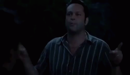 A Man In A Striped Shirt Is Standing In The Dark And Talking . GIF