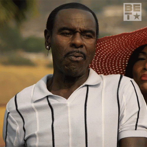 A Man In A Striped Shirt Is Standing Next To A Woman In A Hat GIF
