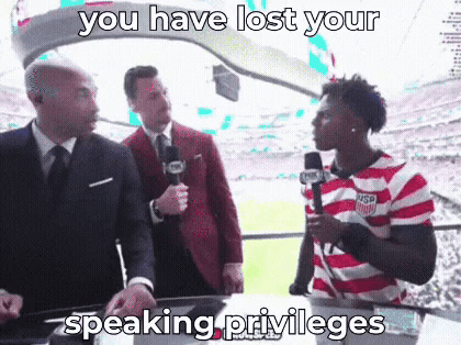 a man in a striped shirt is talking into a microphone while two men in suits look on .