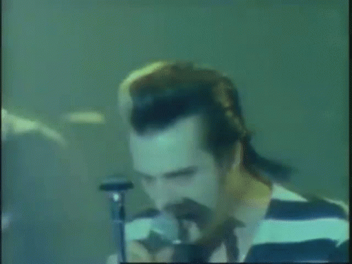 A Man In A Striped Shirt Singing Into A Microphone . GIF