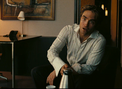 A Man In A Striped Shirt Sits In Front Of A Table GIF