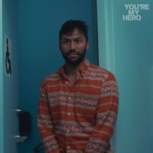 A Man In A Striped Shirt Stands In Front Of A Blue Door With The Words " You 'Re My Hero " Written On It GIF