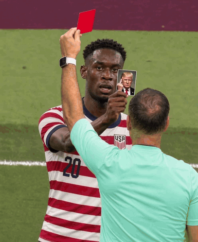 A Man In A Striped Shirt With The Number 20 On It Holds Up A Picture Of Donald Trump GIF