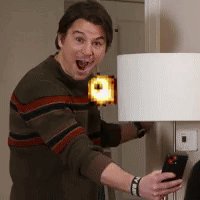 A Man In A Striped Sweater Is Holding A Cell Phone In Front Of A Lamp GIF
