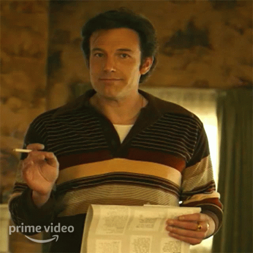 A Man In A Striped Sweater Is Holding A Newspaper And A Cigarette In His Hand . GIF
