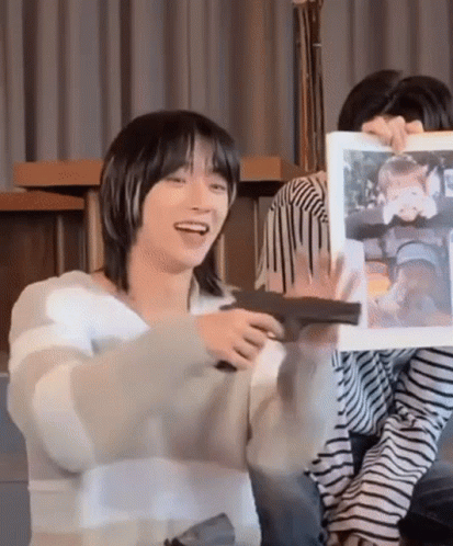 A Man In A Striped Sweater Is Holding A Picture Of A Child And Smiling . GIF