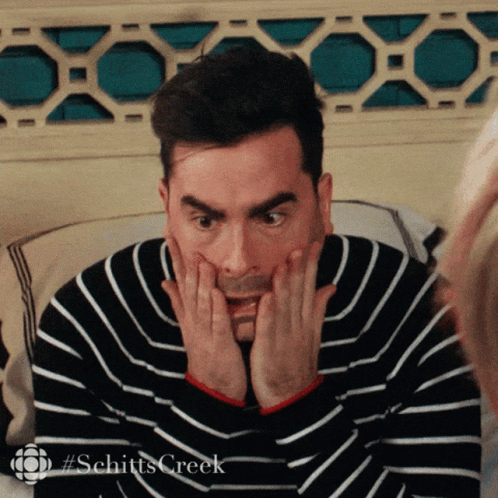 A Man In A Striped Sweater Is Making A Surprised Face With His Hands On His Face . GIF