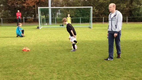 A Man In A Striped Sweatshirt Watches A Boy Kick A Soccer Ball GIF