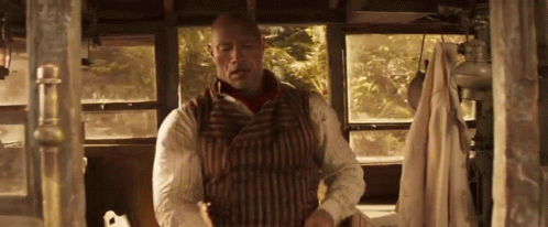 A Man In A Striped Vest Is Standing In A Room With A Window . GIF
