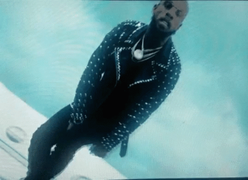 A Man In A Studded Jacket And Sunglasses Is Standing On A Plane GIF