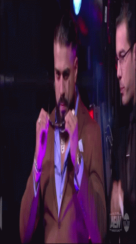 A Man In A Suit Adjusts His Glasses While Another Man Looks On GIF
