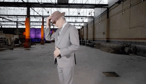 A Man In A Suit Adjusts His Hat In An Empty Building GIF