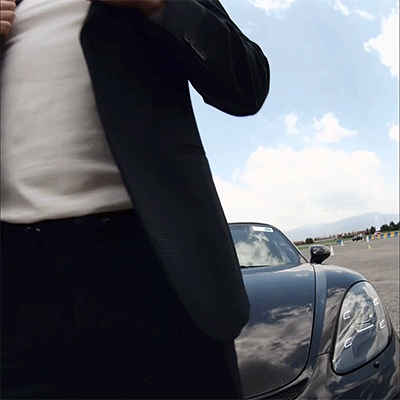 A Man In A Suit Adjusts His Tie In Front Of A Black Sports Car GIF