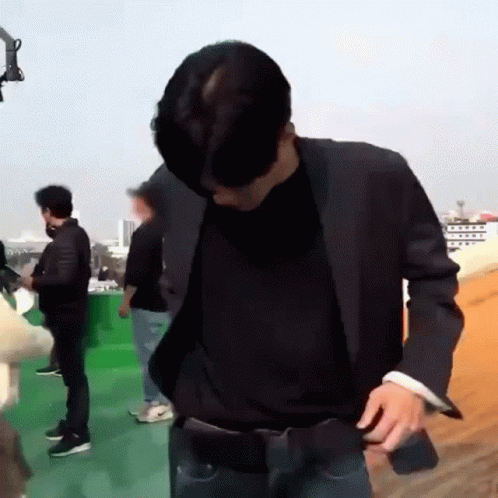 A Man In A Suit And A Black Shirt Is Standing On A Rooftop With Other People . GIF