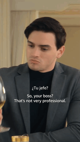 A Man In A Suit And A Black Turtleneck Is Talking To Another Man GIF