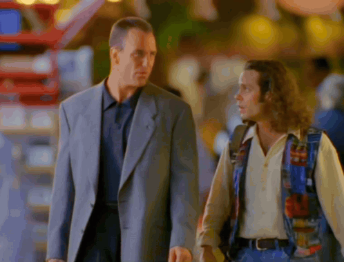 A Man In A Suit And A Man In A Colorful Vest Are Walking Down The Street GIF