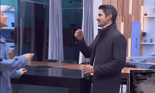 A Man In A Suit And A Woman In A Blue Jacket Are Standing In A Room . GIF