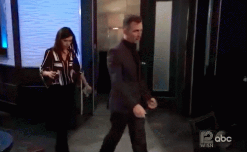 A Man In A Suit And A Woman In A Striped Shirt Are Walking Through A Doorway On Abc . GIF