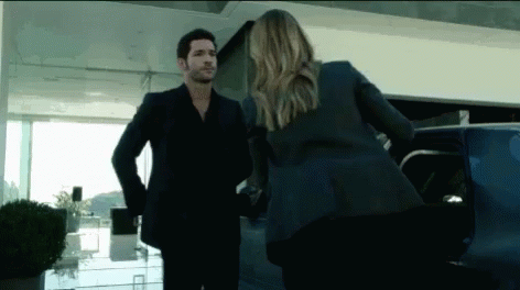 A Man In A Suit And A Woman In A Suit Are Standing Next To Each Other In Front Of A Car . GIF
