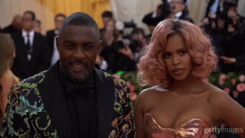 A Man In A Suit And A Woman With Pink Hair Pose For A Photo GIF