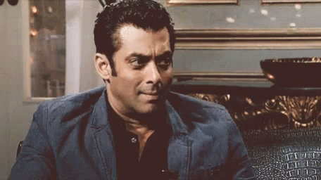 A Man In A Suit And Black Shirt Is Sitting On A Couch And Making A Funny Face . GIF