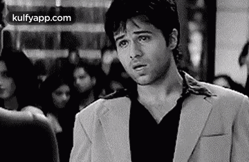 A Man In A Suit And Black Shirt Is Standing In A Crowded Room . GIF