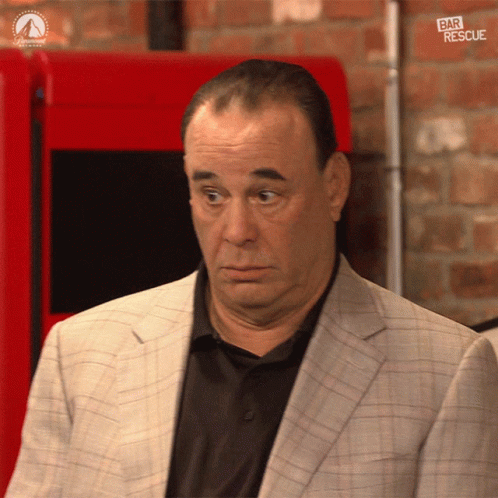 a man in a suit and black shirt is standing in front of a red machine that says bar rescue