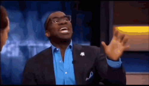 A Man In A Suit And Blue Shirt Is Making A Funny Face While Talking On A Television Show . GIF