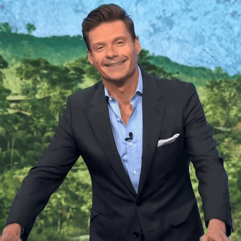 A Man In A Suit And Blue Shirt Is Smiling In Front Of A Green Background GIF