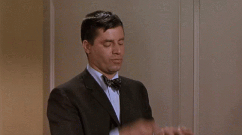 A Man In A Suit And Bow Tie Is Adjusting His Cuffs . GIF