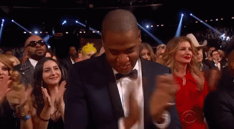 A Man In A Suit And Bow Tie Is Dancing In Front Of A Crowd Of People GIF