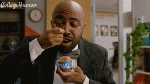 A Man In A Suit And Bow Tie Is Eating From A Jar Of Baby Food GIF