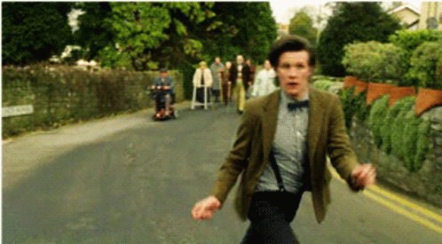 A Man In A Suit And Bow Tie Is Running Down The Street GIF