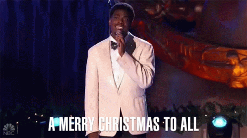 A Man In A Suit And Bow Tie Is Singing Into A Microphone And Saying A Merry Christmas To All . GIF