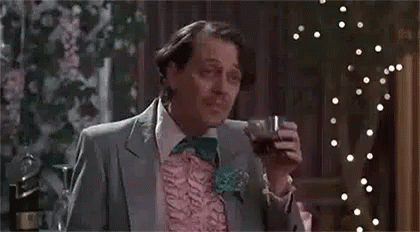 A Man In A Suit And Bow Tie Is Sitting At A Table Holding A Glass Of Wine . GIF
