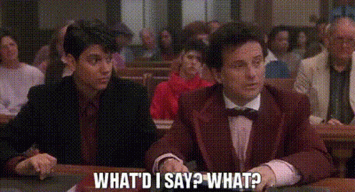 A Man In A Suit And Bow Tie Is Sitting At A Table In Front Of A Crowd Of People . GIF